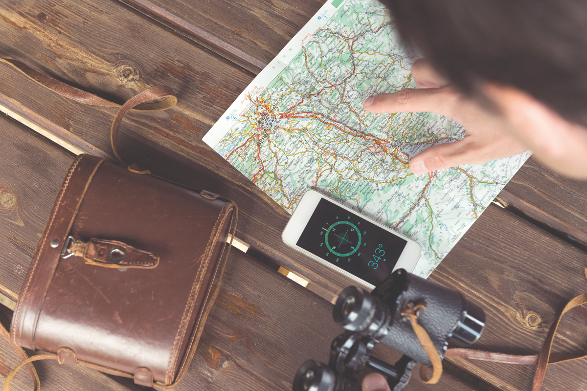 Bild einer Landkarte, eines Kompasses am Smartphone und einem Fernglas, das auf einem Holztisch liegt