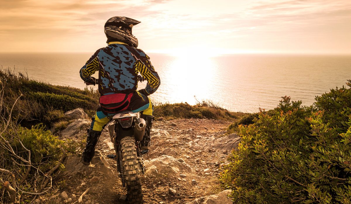 Motocrossfahrer vor Steilküste mit Blick auf das Meer
