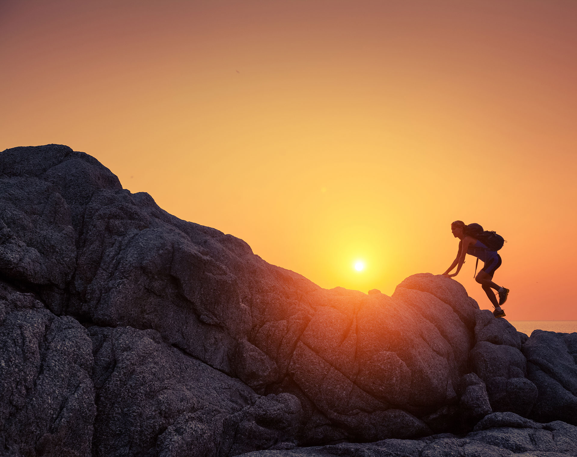 Bild einer Wanderin auf einem Felsmassiv bei Sonnenaufgang